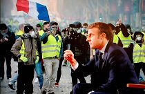 الرئيس الفرنسي إيمانويل ماكرون أمام صورة لاحتجاجات السترات الصفراء.