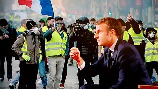 الرئيس الفرنسي إيمانويل ماكرون أمام صورة لاحتجاجات السترات الصفراء. 