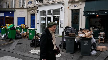 An elderly woman man walks past not collected garbage cans, Thursday, March 9, 2023 in Paris.