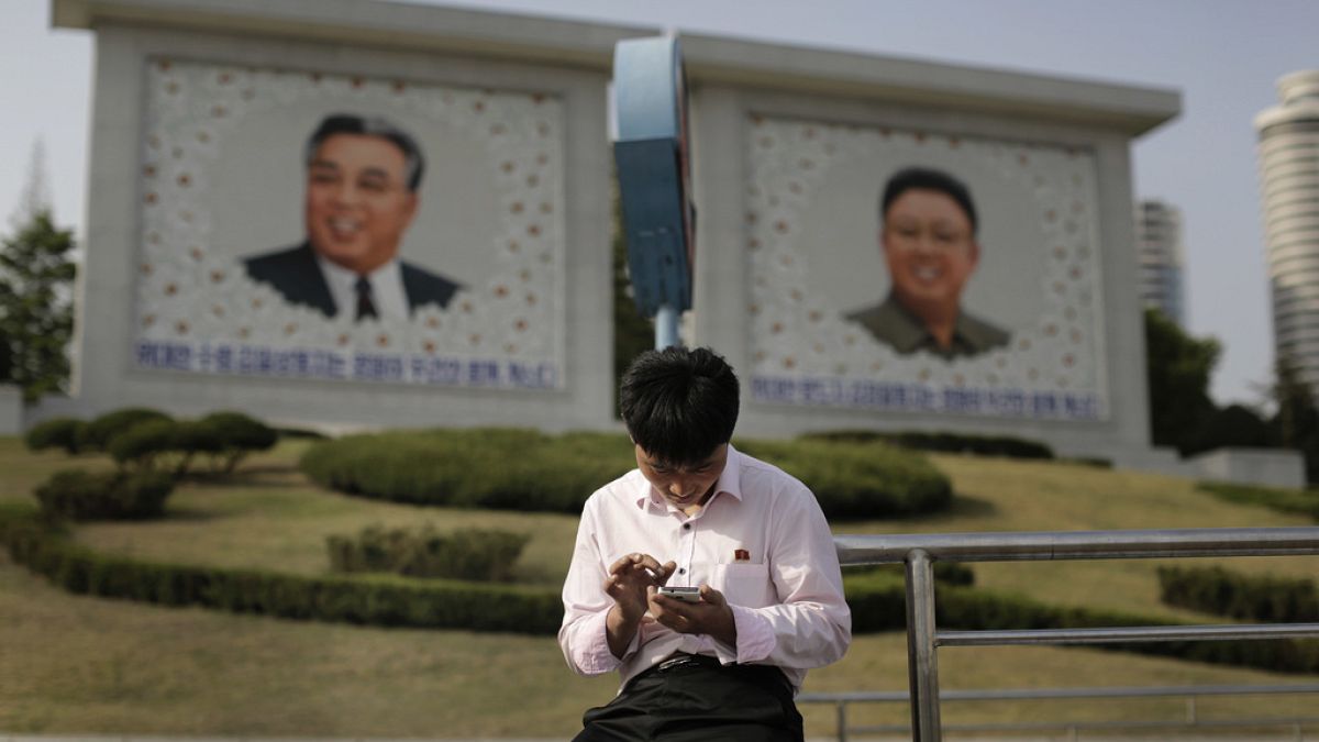 Észak-koreai férfi telefonozik Kim Ir Szen és Kim Dzsong Il portréja előtt