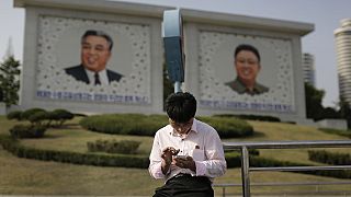 Észak-koreai férfi telefonozik Kim Ir Szen és Kim Dzsong Il portréja előtt
