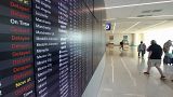 Passengers walk past s flight status board in Terminal C at Orlando International Airport that shows many delays