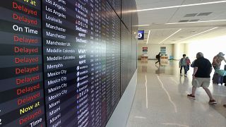 Passengers walk past s flight status board in Terminal C at Orlando International Airport that shows many delays