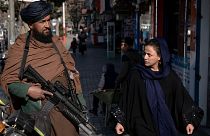 یک زن افغان در حال عبور از کنار یک نیروی امنیتی طالبان در خیابانی در کابل به تاریخ ۲۶ دسامبر ۲۰۲۲