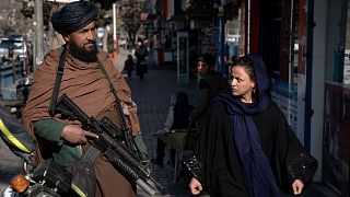 یک زن افغان در حال عبور از کنار یک نیروی امنیتی طالبان در خیابانی در کابل به تاریخ ۲۶ دسامبر ۲۰۲۲