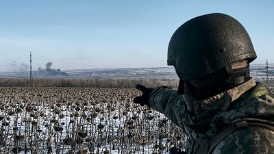 Soldado ucraniano aponta para coluna de fumo na linha da frente em Soledar