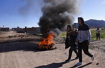 Residents walk past a burning roadblock set up by anti-government protesters in Desaguadero, Peru, on the border with Bolivia, 13 January, 2023.