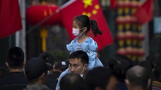A girl wearing a face mask rides on a man's shoulders as they walk along a tourist shopping street in Beijing, 7 October 2022