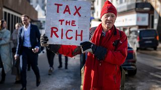 هيل وايت، مليونير بريطاني يقف مع لافتة كتب عليها: "إفرضوا ضرائب على الأغنياء" بجوار مقر الاجتماع السنوي لمنتدى في دافوس في سويسرا، في 18 يناير/كامون الثاني 2023. 