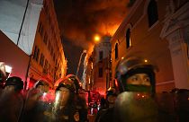 Policías antidisturbios bloquean una calle mientras un edificio arde tras ellos tras un día de enfrentamientos con manifestantes antigubernamentales en Lima, Perú.