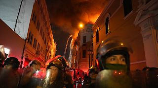 Policías antidisturbios bloquean una calle mientras un edificio arde tras ellos tras un día de enfrentamientos con manifestantes antigubernamentales en Lima, Perú.