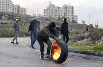 متظاهر فلسطيني يلقي بإطار محترق على قوات الأمن الإسرائيلي وسط مواجهات عند المدخل الشمالي لمدينة رام الله بالقرب من مستوطنة بيت إيل الإسرائيلية، في 20 ديسمبر 2022