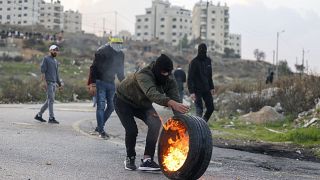 متظاهر فلسطيني يلقي بإطار محترق على قوات الأمن الإسرائيلي وسط مواجهات عند المدخل الشمالي لمدينة رام الله بالقرب من مستوطنة بيت إيل الإسرائيلية، في 20 ديسمبر 2022 