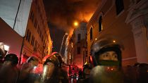 Police in riot gear block a street as a building burns behind them after a day a day of clashes with anti-government protesters in Lima, Peru. Thursday, 19 Jan. 2023.