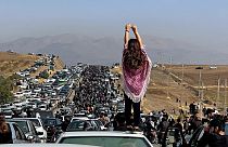 An Iranian woman stands on top of a car. 