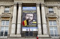 A Belgian flag flutters in front of a banner asking to free Belgian aid worker Olivier Vandecasteele, currently detained in Iran, in Brussels, Belgium, Sunday, Jan. 22, 2023. 