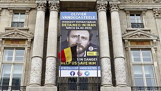 A Belgian flag flutters in front of a banner asking to free Belgian aid worker Olivier Vandecasteele, currently detained in Iran, in Brussels, Belgium, Sunday, Jan. 22, 2023. 