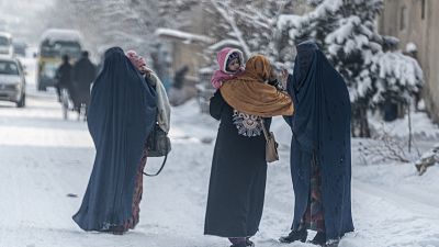 نساء أفغانيات يرتدين البرقع يحملن أطفالهن أثناء سيرهن في شارع مليء بالثلوج في العاصمة كابول، 23 يناير 2023.
