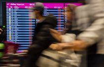 Passengers walk past the display board showing all flights as canceled during a warning strike at Berlin-Brandenburg BER Airport in Schoenefeld, Germany, Jan. 25, 2023