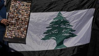 لبنانية تحمل صوراً لضحايا انفجار مرفأ بيروت 2020 بجانب العلم اللبناني خلال احتجاج أمام قصر العدل، بيروت، لبنان 2023