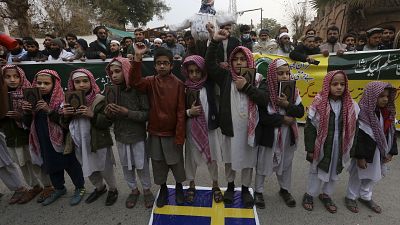أطفال يحملون "القرآن" ويقفون فوق علم السويد خلال مظاهرة في بيشاور، باكستان.