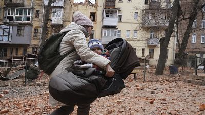 أم تنقل ابنها الصغير من المبنى السكني حيث تسكن العائلة في خاركيف بعد قصف روسي 