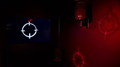 Dentro da caixa reina a escuridão absoluta, interrompida por luzes vermelhas intermitentes e símbolos de alvos pintados à mão
