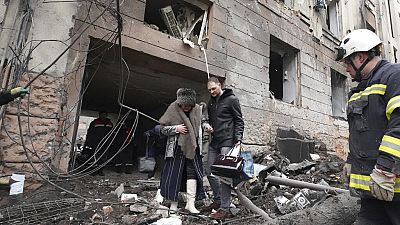 Un homme aide une habitante de Kharkik à sortir de son immeuble touché par une frappe russe, 5 février 2023