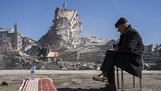 Ein Mann im südtürkischen Nurdagi sitzt auf einem Stuhl. Hinter ihm sind die Gebäude wie Kartenhäuser zusammengefallen.