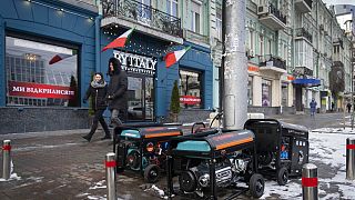 People pass by working generators during a power outage in Kyiv, Ukraine, Monday, Feb. 6, 2023.