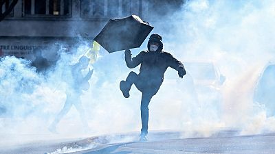A protester with an umbrella kicks away a teargas pellet during a demonstration on the third day of nationwide rallies