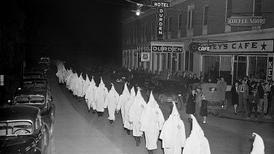 Members of the Ku Klux Klan, wearing traditional white hoods and robes, march in single file 