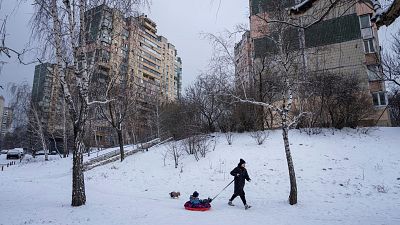 سيدة أوكرانية تجر ابنها وهو يركب على مزلاج على الثلوج في ضواحي العاصمة كييف