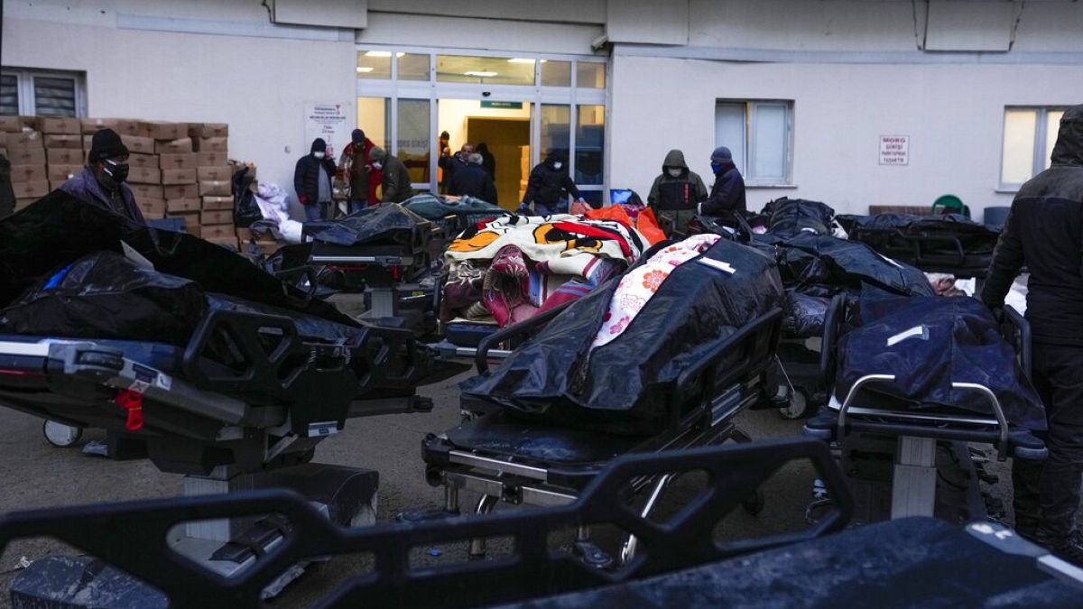 People stand next to the dead bodies of earthquake victims at a hospital in Turkey, Thursday, Feb. 9, 2023