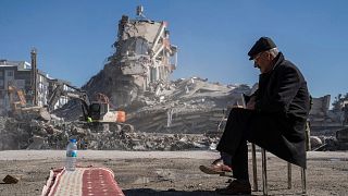 Mehmet Nasir Duran, 67, sits on a chair, as heavy machines remove debris from a building, where five of his family members are trapped in Nurdagi, southeastern Turkey.