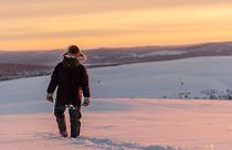 A reindeer herder walks across the snow as the sun sets near Kiruna, Sweden.