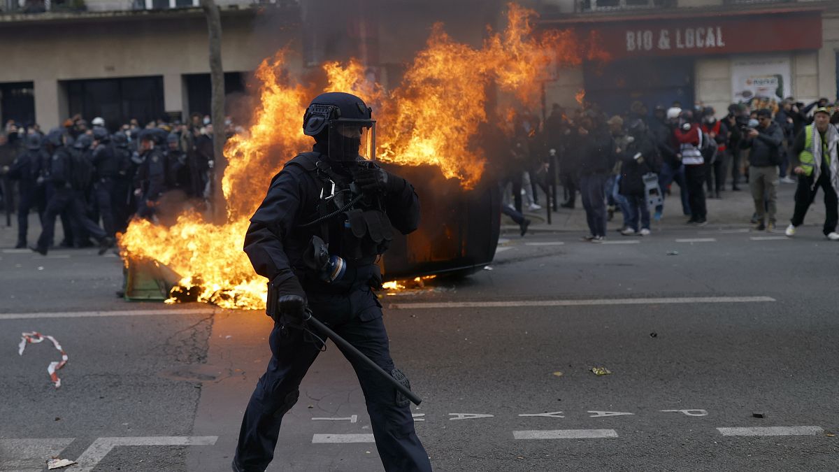 A francia kormány tervezett nyugdíjreformja ellen tüntetők által felgyújtott autó előtt egy rohamrendőr Párizsban 2023. február 11-én.