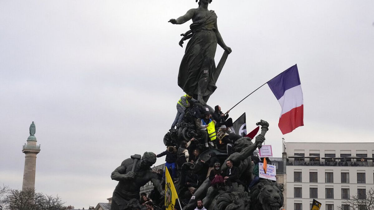 Protesters stand on top of Place de la Nation statue at the end of a demonstration against plans to push back France's retirement age, in Paris, Saturday, Feb. 11, 2023.