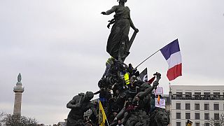 Protesters stand on top of Place de la Nation statue at the end of a demonstration against plans to push back France's retirement age, in Paris, Saturday, Feb. 11, 2023.