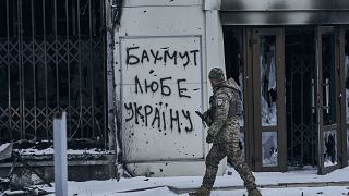 A Ukrainian soldier walks along a street in Bakhmut, Donetsk region, Ukraine, Sunday, Feb. 12, 2023. Writing on the wall reads "Bakhmut loves Ukraine". 