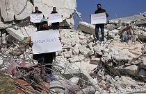 Des Syriens se tiennent au milieu des décombresavec des pancartes critiquant l'ONU, 12 février 2023. 