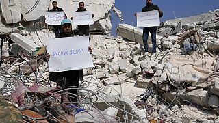 Des Syriens se tiennent au milieu des décombresavec des pancartes critiquant l'ONU, 12 février 2023. 