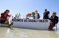 People holding a "business as usual" sign on the tide. 