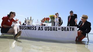 People holding a "business as usual" sign on the tide. 