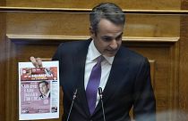 Greece's Prime Minister Kyriakos Mitsotakis holds a copy of a Greek newspaper's front page during his speech at the parliament in Athens, Greece, Aug. 26, 2022.