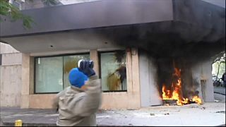 Un hombre con una piedra en mano en la entrada de un banco incendiado