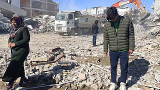 Taha Erdem (r), his mother Zeliha Erdem (l) and father Ali Erdem stand next to the debris from a building where Tahan was trapped after the earthquake in Adiyaman, Turkey.