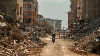 مردی سوار بر موتورسیکلت از کنار آوار ساختمان های ویران شده در سمندغ، جنوب ترکیه، چهارشنبه، ۲۲ فوریه ۲۰۲۳.