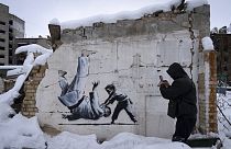 Ein Mann fotografiert ein Banksy-Kunstwerk an einem zerstörten Gebäude in Borodyanka, Region Kiew, Ukraine