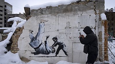 Ein Mann fotografiert ein Banksy-Kunstwerk an einem zerstörten Gebäude in Borodyanka, Region Kiew, Ukraine